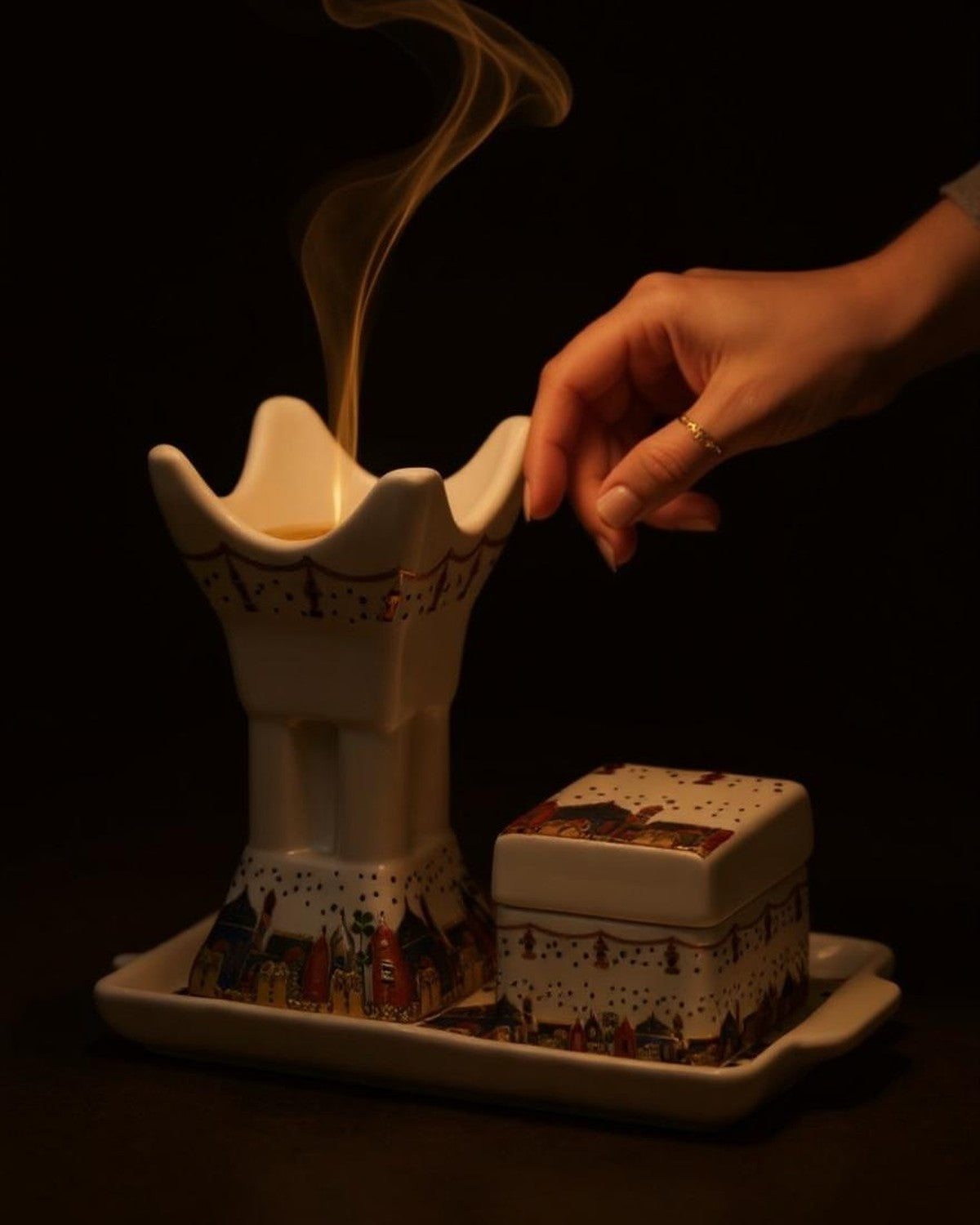 ZYVORA Mabkhara — placing bakhoor onto the warm cradle. Smoke threads through the room.